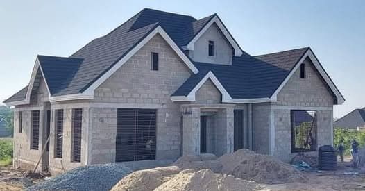 Single-storey house at roofing stage, with a completed pitched tiled roof over unrendered block walls and framed window openings